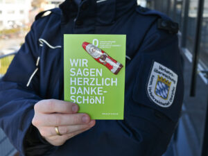 Das Bild zeigt einen grünen Flyer, der an eine Autowindschutzscheibe gesteckt ist. Auf dem Flyer steht "Wir danke Dankeschön", zudem ist ein kleiner Schokoladennikolaus auf die Karte geklebt.